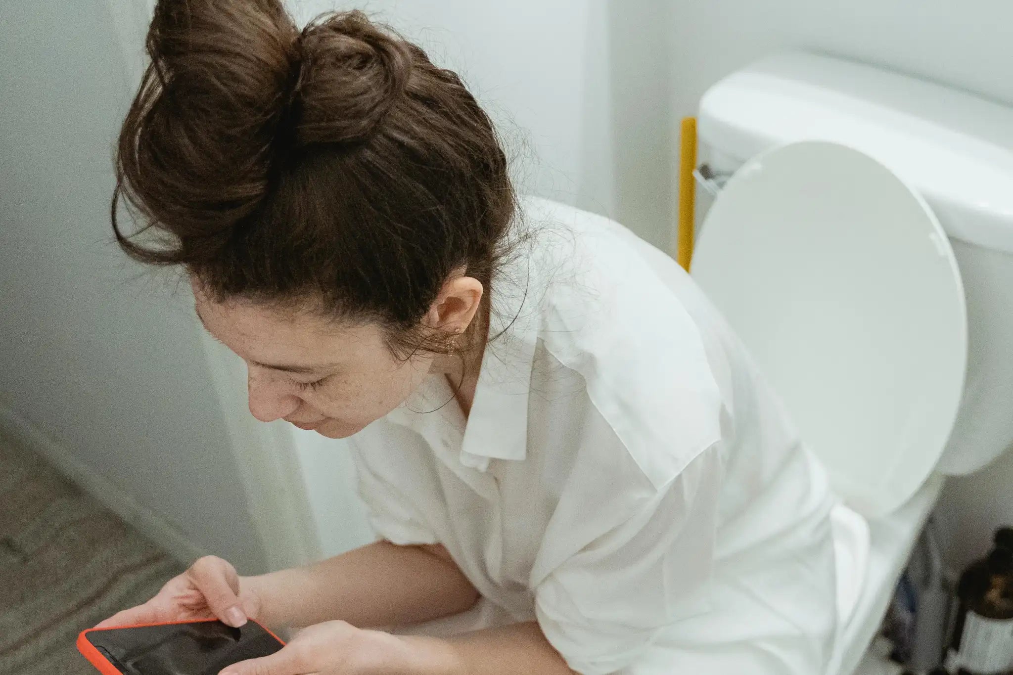 A person sitting on the toilet, playing with their phone