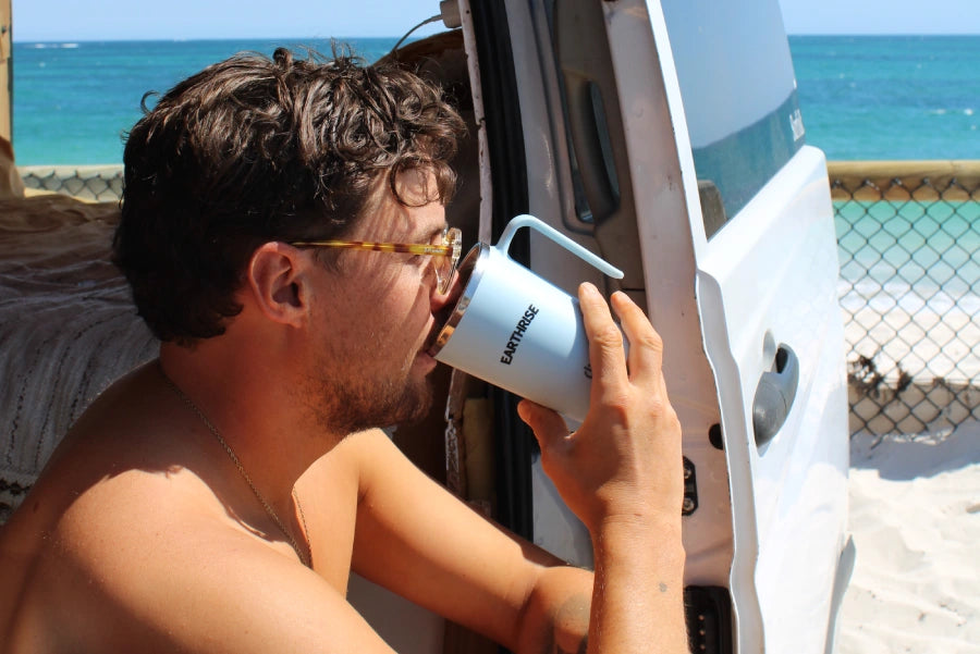 A person drinking from an Earthrise mug, sitting on the beach